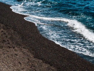 黒い砂浜に白い波が打ち寄せる波打ち際