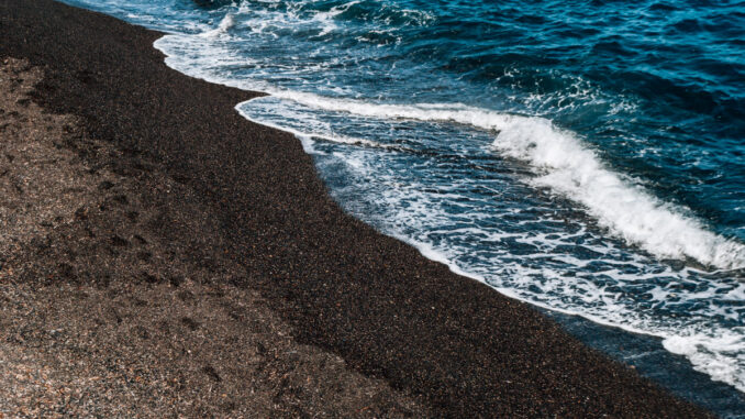 黒い砂浜に白い波が打ち寄せる波打ち際