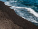 黒い砂浜に白い波が打ち寄せる波打ち際